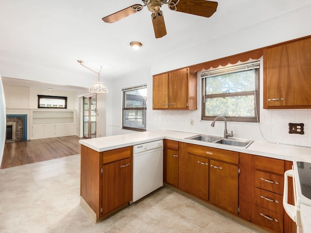 kitchen featuring sink, dishwasher, hanging light fixtures, a stone fireplace, and kitchen peninsula