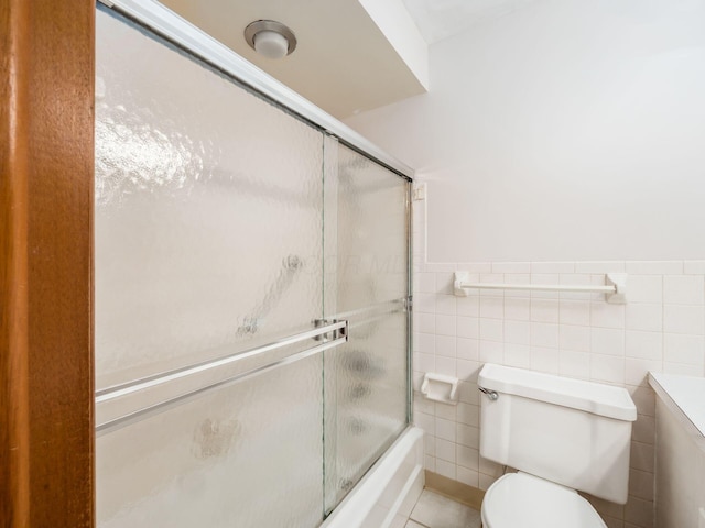 bathroom featuring tile patterned floors, toilet, combined bath / shower with glass door, and tile walls