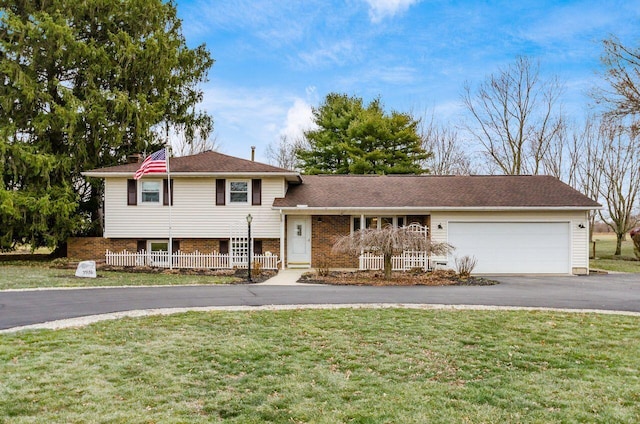 tri-level home with aphalt driveway, an attached garage, brick siding, and a front lawn