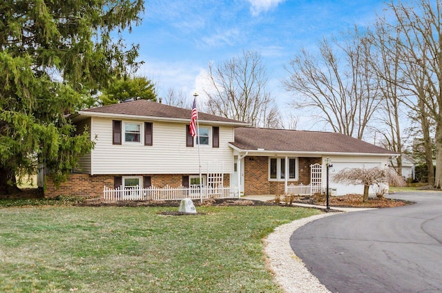 split level home featuring a front yard, brick siding, an attached garage, and driveway