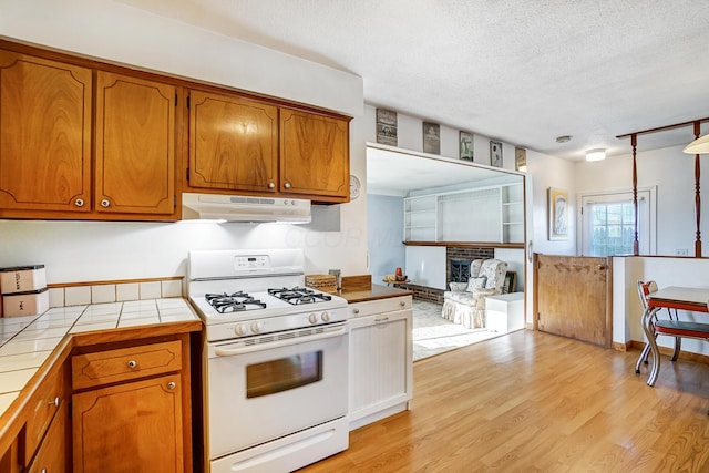 kitchen featuring light hardwood / wood-style flooring, a fireplace, a textured ceiling, tile countertops, and white gas stove