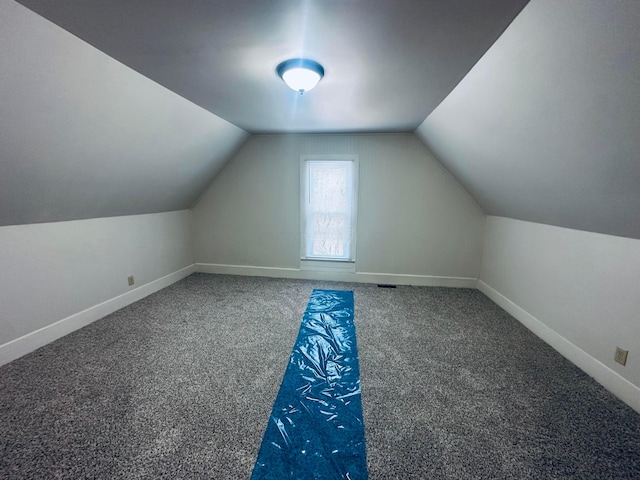 additional living space featuring vaulted ceiling and dark colored carpet