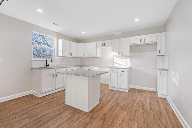 kitchen with baseboards, decorative backsplash, white cabinets, light wood-type flooring, and a sink