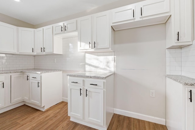 kitchen with light stone counters, light wood-type flooring, white cabinetry, and tasteful backsplash