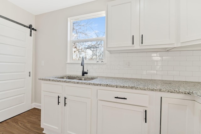 kitchen with a barn door, dark wood-type flooring, a sink, white cabinetry, and tasteful backsplash