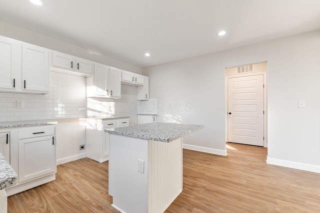 kitchen with a center island, white cabinetry, backsplash, and light wood finished floors