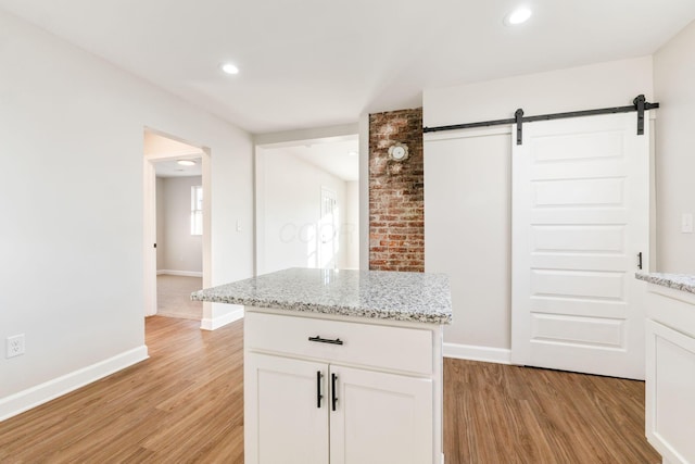 kitchen with light stone countertops, a barn door, white cabinetry, and light wood-style flooring