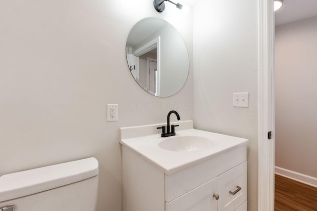 half bath featuring toilet, baseboards, wood finished floors, and vanity