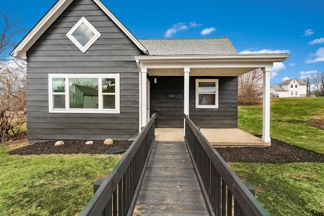 view of front of house with covered porch, roof with shingles, and a front lawn