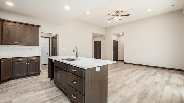 kitchen with tasteful backsplash, dark brown cabinets, sink, and a center island with sink