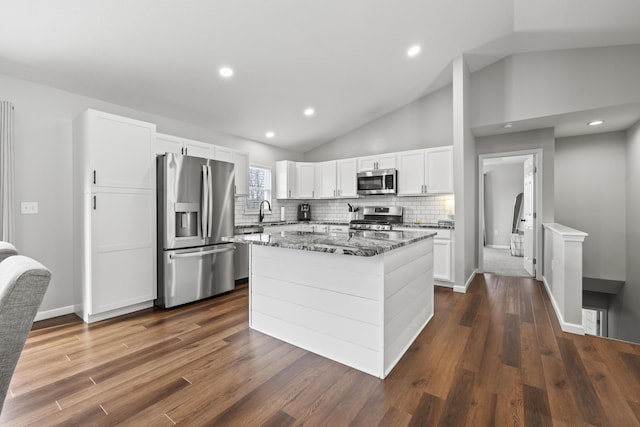 kitchen with dark stone countertops, backsplash, stainless steel appliances, a center island, and white cabinets