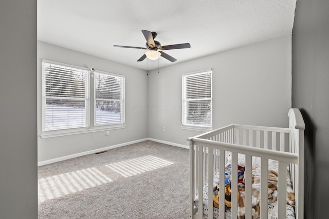 unfurnished bedroom featuring a crib, carpet flooring, and ceiling fan