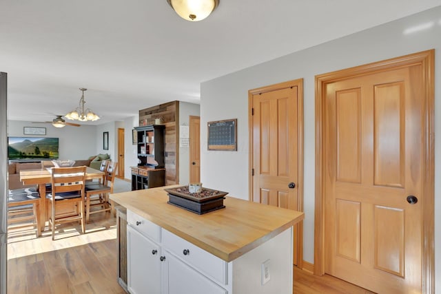 kitchen featuring decorative light fixtures, butcher block counters, white cabinets, a center island, and light wood-type flooring