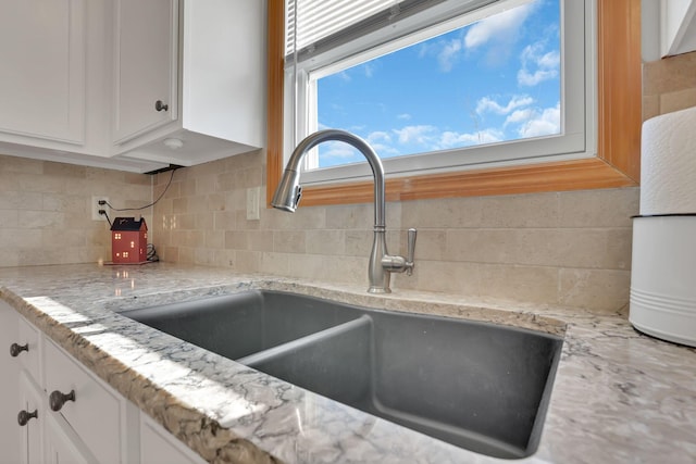 interior details with white cabinetry, sink, light stone counters, and tasteful backsplash