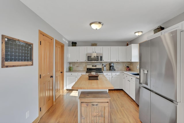 kitchen featuring white cabinetry, backsplash, stainless steel appliances, light hardwood / wood-style floors, and a kitchen island