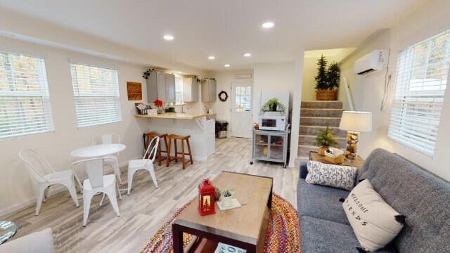 living room with a wall mounted air conditioner and light wood-type flooring