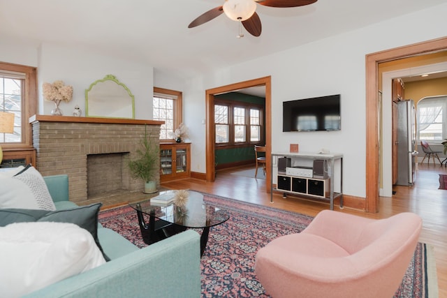 living room with ceiling fan, wood-type flooring, and a brick fireplace