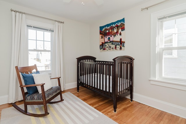 bedroom with hardwood / wood-style flooring, a nursery area, and ceiling fan