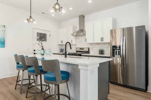 kitchen with an island with sink, appliances with stainless steel finishes, sink, and wall chimney range hood