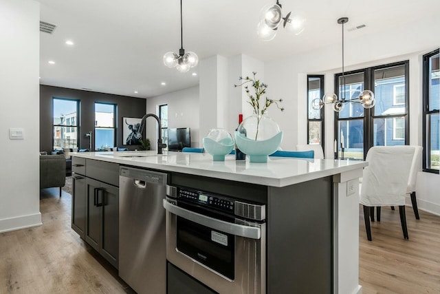 kitchen featuring hanging light fixtures, appliances with stainless steel finishes, a center island with sink, and a chandelier