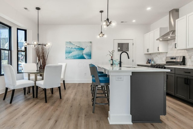 kitchen featuring pendant lighting, sink, a kitchen island with sink, stainless steel range, and wall chimney exhaust hood