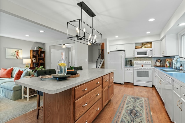 kitchen with white appliances, white cabinets, a breakfast bar, open floor plan, and light countertops