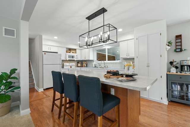 kitchen with white appliances, visible vents, white cabinets, a center island, and light countertops