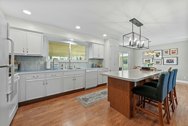 kitchen featuring a center island, light countertops, white cabinets, a sink, and white appliances