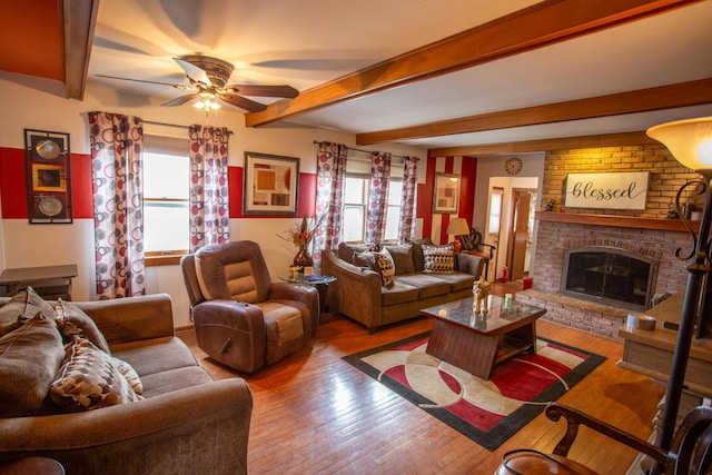 living room with ceiling fan, beam ceiling, a brick fireplace, and light hardwood / wood-style flooring