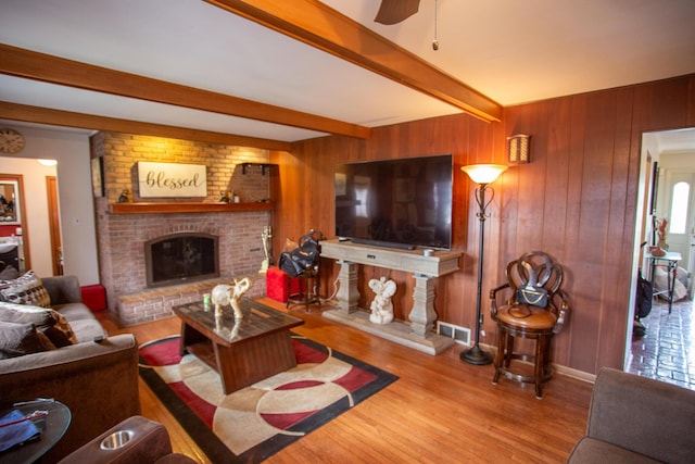 living room featuring a brick fireplace, wood walls, beamed ceiling, and light wood-type flooring