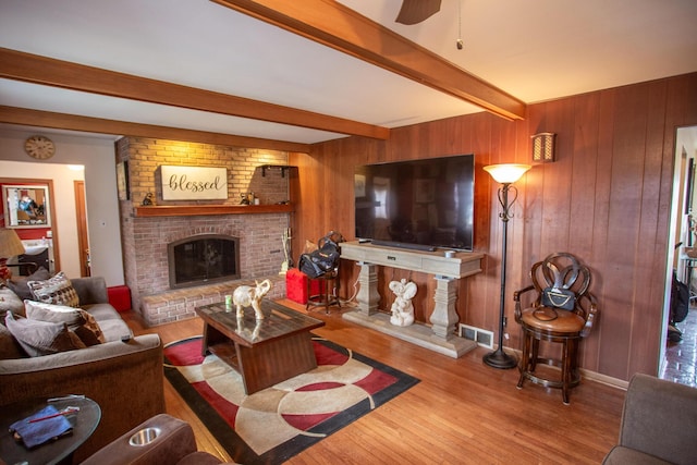 living room featuring a brick fireplace, wood walls, beamed ceiling, and light wood-type flooring