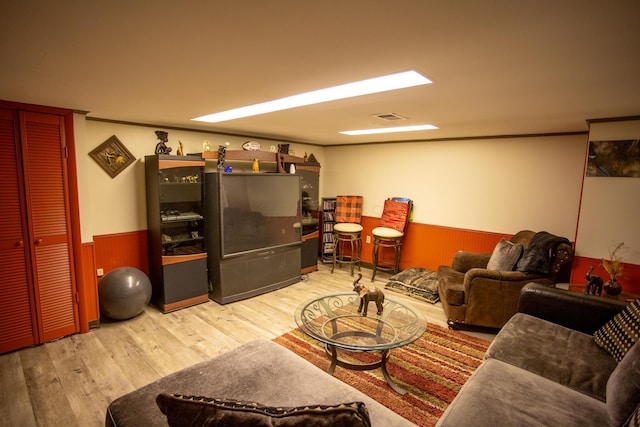 living room with crown molding, wooden walls, and light hardwood / wood-style flooring