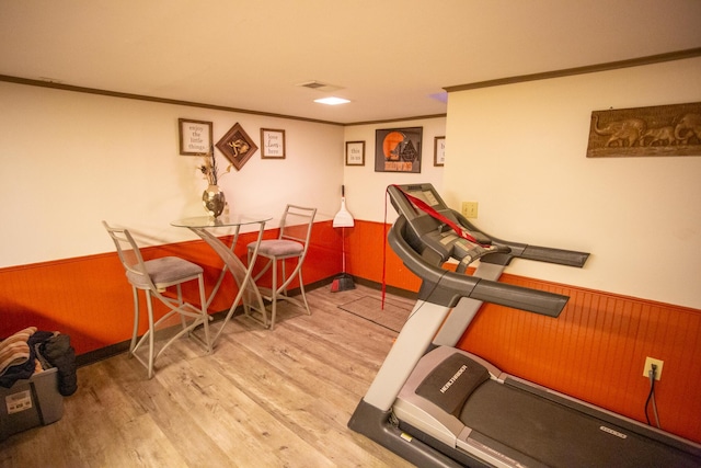 workout area featuring ornamental molding, light hardwood / wood-style floors, and wood walls