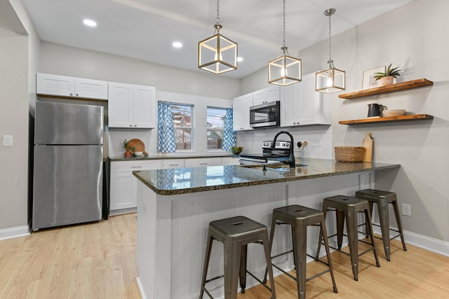 kitchen featuring white cabinetry, stainless steel appliances, decorative light fixtures, and a kitchen breakfast bar