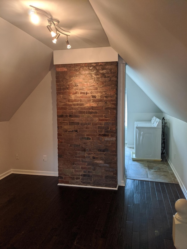 bonus room with dark wood-type flooring, independent washer and dryer, brick wall, and vaulted ceiling