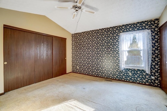 unfurnished bedroom featuring ceiling fan, lofted ceiling, carpet floors, and a closet