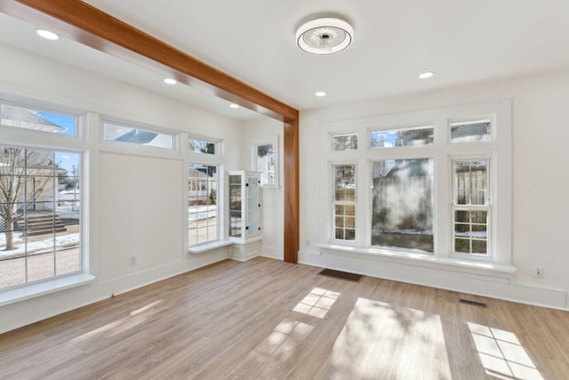 unfurnished living room featuring beam ceiling, a healthy amount of sunlight, and light wood-type flooring