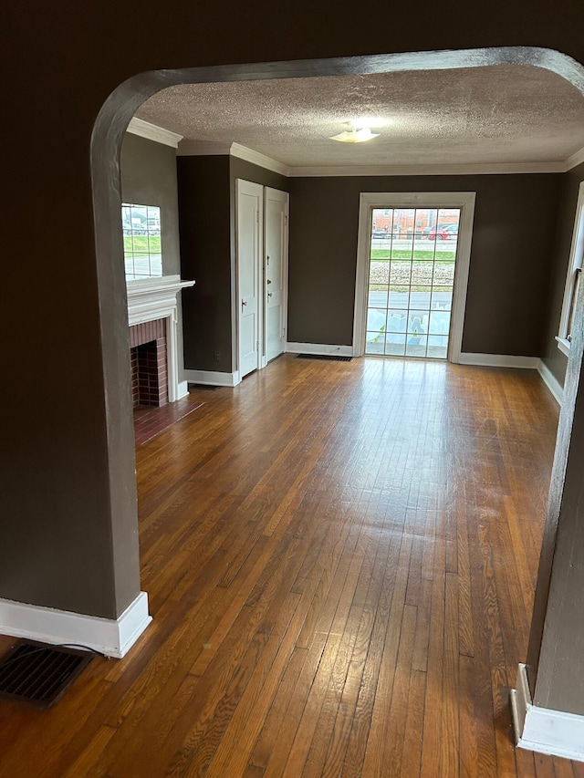 unfurnished living room featuring dark hardwood / wood-style floors, ornamental molding, a fireplace, and a textured ceiling