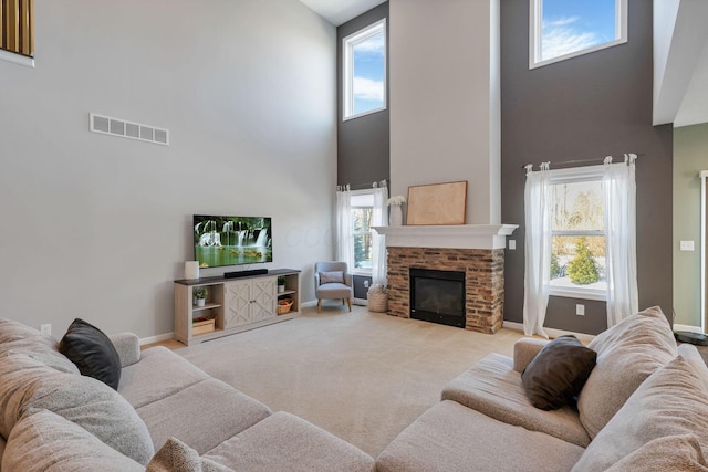 living room featuring light carpet, a towering ceiling, a stone fireplace, and a healthy amount of sunlight