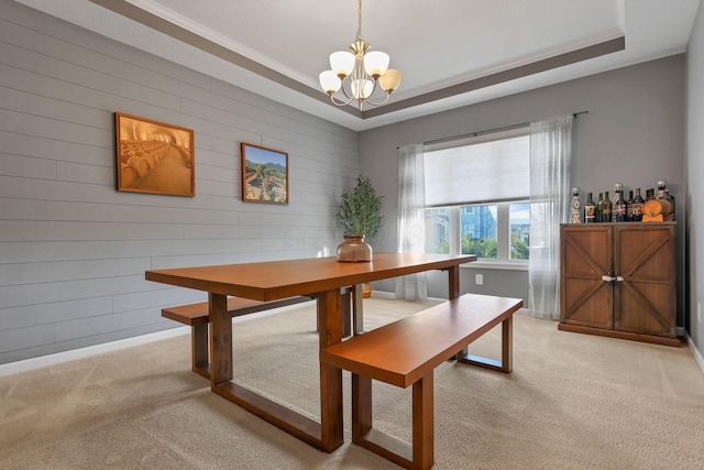 carpeted dining area featuring ornamental molding, an inviting chandelier, and a tray ceiling