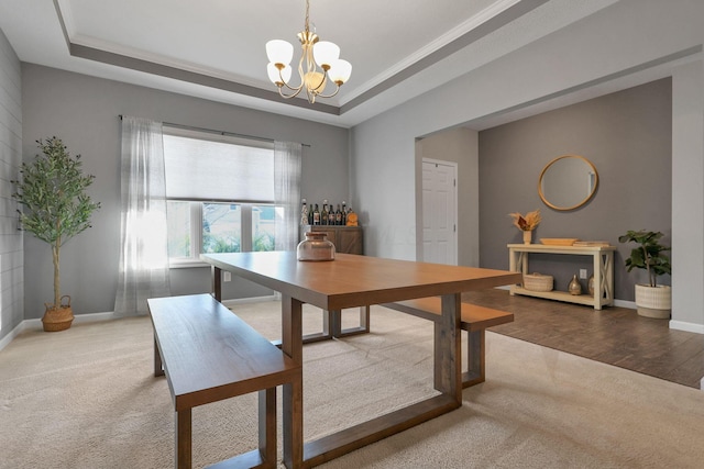 carpeted dining space with an inviting chandelier, a tray ceiling, and crown molding