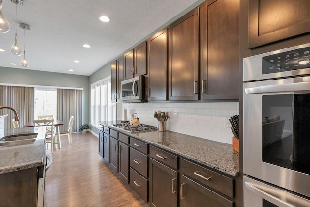 kitchen with stainless steel appliances, decorative light fixtures, sink, and dark stone counters