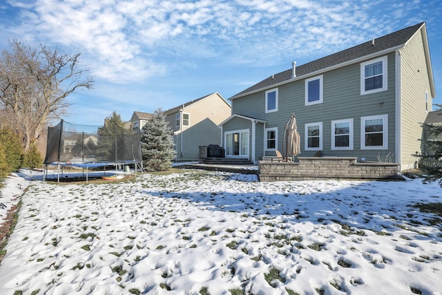 snow covered back of property featuring a trampoline