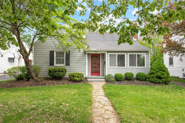 view of front of property featuring a shingled roof, a chimney, and a front yard