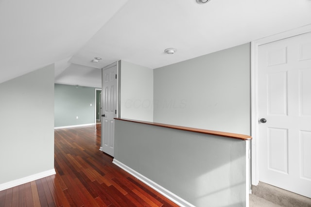 hallway featuring lofted ceiling, wood-type flooring, and baseboards