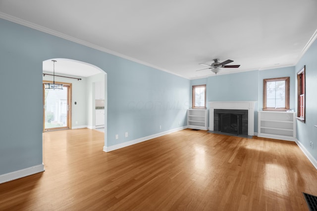 unfurnished living room with wood finished floors, arched walkways, a ceiling fan, baseboards, and a fireplace with flush hearth