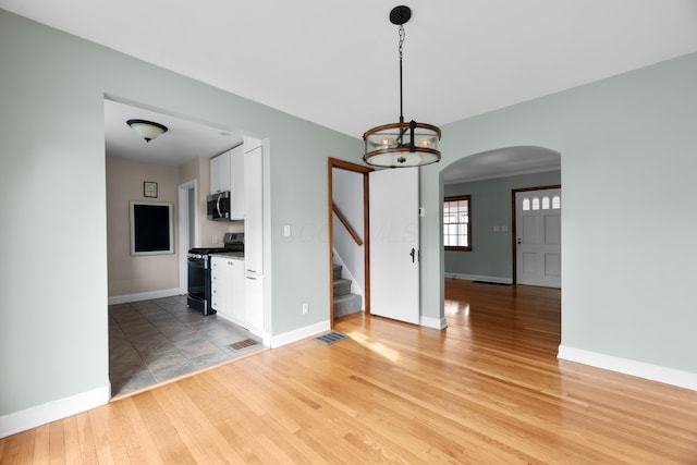 interior space with light wood-type flooring, stairway, baseboards, and arched walkways