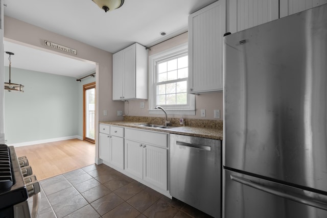 kitchen with dark tile patterned floors, a sink, white cabinets, baseboards, and appliances with stainless steel finishes