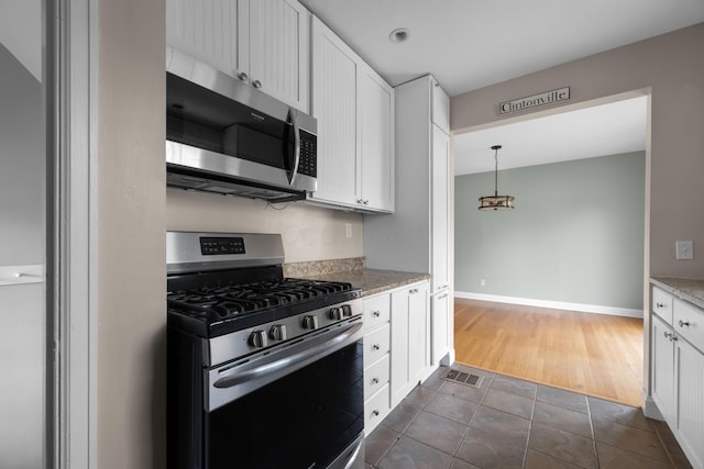 kitchen with stainless steel appliances, dark tile patterned flooring, light stone counters, and white cabinets