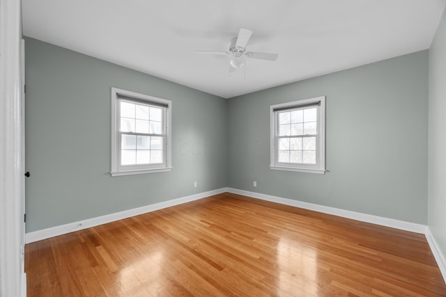 empty room featuring light wood-style flooring, baseboards, a ceiling fan, and a healthy amount of sunlight